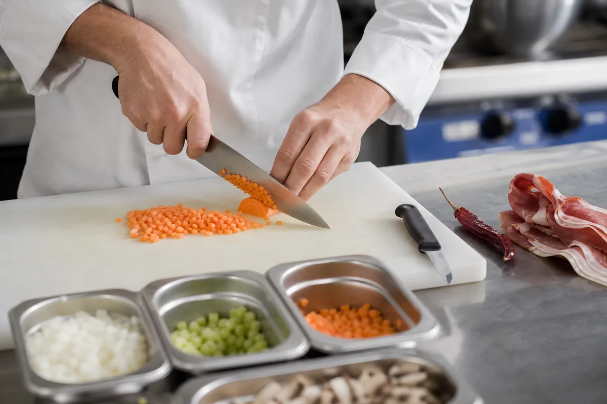 Apprenti cuisinier en veste blanche à la mise en place dans une cuisine professionnelle